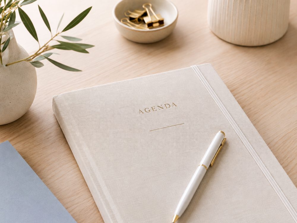 Agenda, stylo doré et brin d'olivier sur un bureau en bois clair